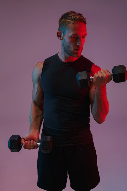Concentrated young sports man make exercises with dumbbells. - Foto, imagen