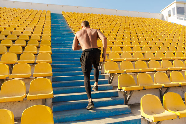 Image of sportsman running by empty stadium seats while doing wo - Foto, afbeelding