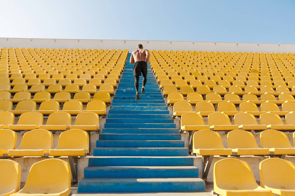 Image of athletic sportsman running by stadium seats while doing - Foto, afbeelding