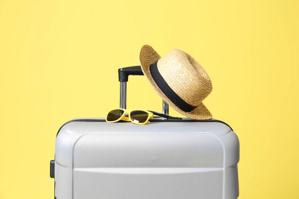 Grey suitcase with sunglasses and hat on yellow background - Foto, Bild