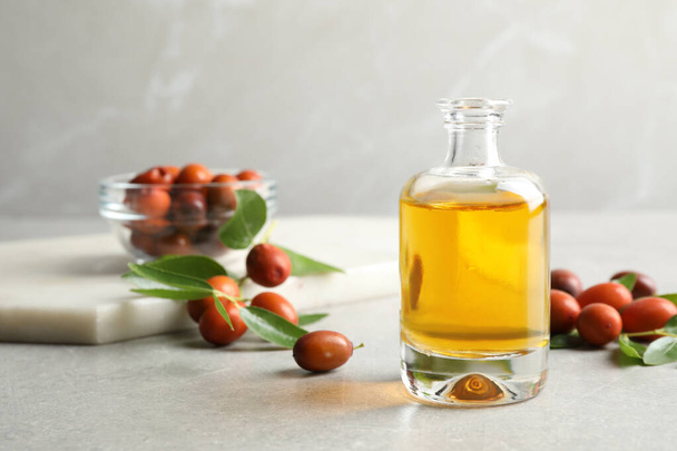 Jojoba oil in glass bottle and seeds on light grey table - Foto, Imagen