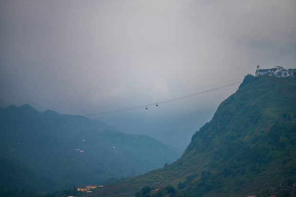 Um teleférico correndo da cidade de Sapa, no Vietnã, em direção às montanhas da Indochina durante a madrugada com nevoeiro e nuvens no fundo
 - Foto, Imagem