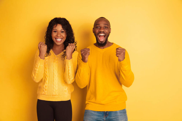 Young emotional african-american man and woman on yellow background - Φωτογραφία, εικόνα