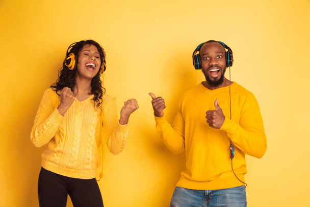Young emotional african-american man and woman on yellow background - 写真・画像