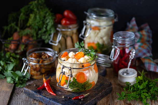 Coliflor en escabeche con zanahorias en un frasco de vidrio sobre una mesa de madera oscura. Alimentos fermentados
. - Foto, Imagen