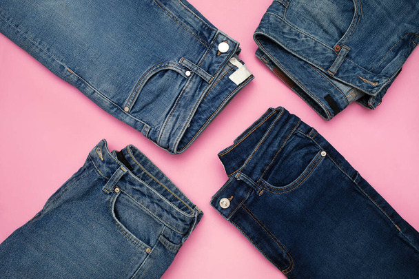Several pairs of blue denim jeans on pink background - Foto, afbeelding