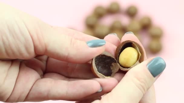 Two hands shelling raw not peeled whole macadamia nuts on pink background with special instrument. Healthy food. Protein source. View from above. - Footage, Video