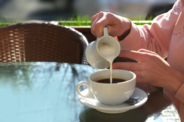 Woman pouring milk in coffee at table in cafe - Foto, immagini