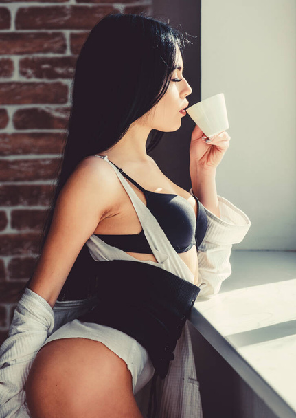 Coffee, take me away. Sensual girl drinking her favorite morning coffee. Pretty woman drinking fresh hot coffee at window. Sexy girl holding ceramic coffee cup - 写真・画像