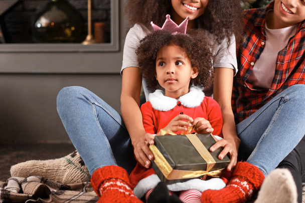 Happy African-American family with gift at home on Christmas eve - 写真・画像