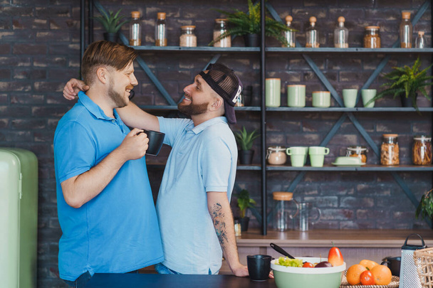 glückliches schwules Paar in der Küche. Männer trinken Tee und umarmen sich - Foto, Bild