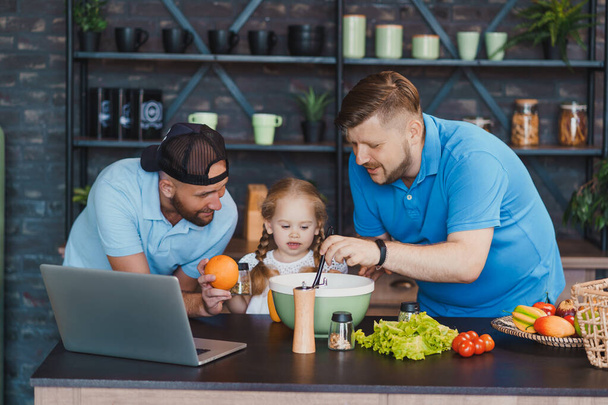 Gay parents cooking with their child and looking a recipe on a laptop - Foto, immagini