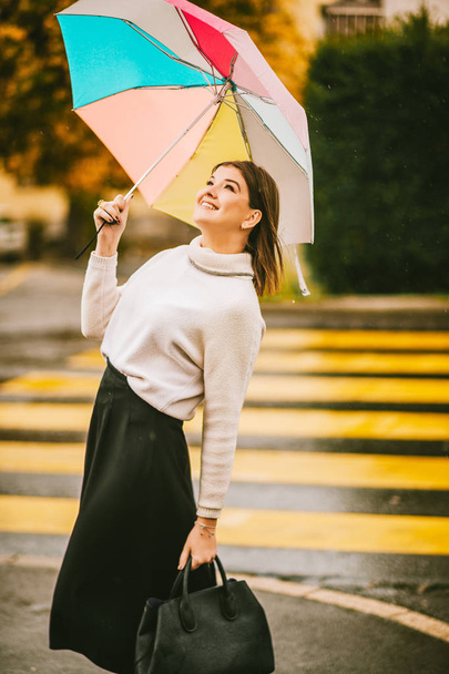 Stylish young woman under the rain, holding colorful umbrella, wearing warm pullover and black skirt - Photo, Image