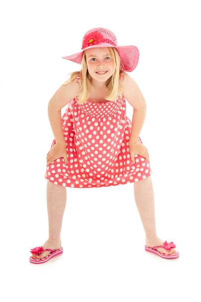 Πλήρες πλάνο του όμορφου ξανθού κοριτσιού με μεγάλο ροζ καπέλο, πουά φόρεμα και σαγιονάρες. Απομονωμένο σε λευκό φόντο στούντιο - Φωτογραφία, εικόνα