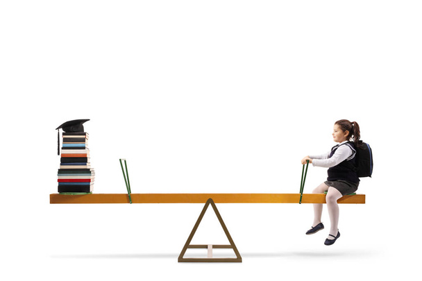Schoolgirl sitting on one side of a seesaw and a pile of books w - Fotoğraf, Görsel