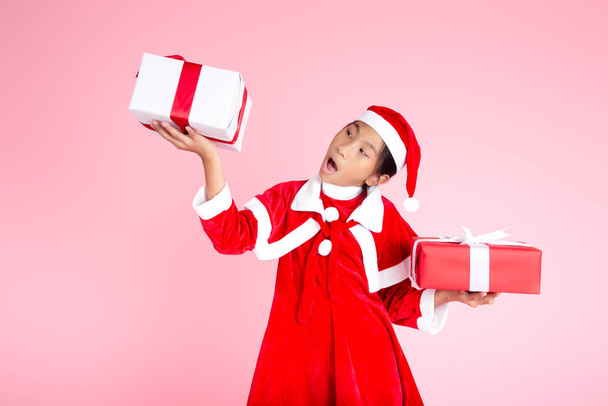 Happy Asian girl in Christmas costume holding gift box on pink b - Foto, imagen