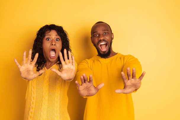 Young emotional african-american man and woman on yellow background - Fotoğraf, Görsel