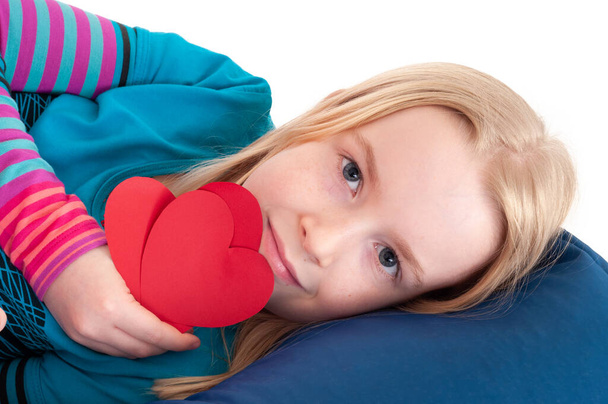 Close up of pretty young blonde girl holding red paper hearts in front of her while lay down - Photo, Image