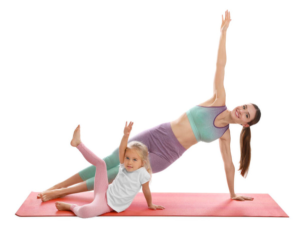 Young woman and her daughter doing exercise isolated on white. Home fitness - 写真・画像