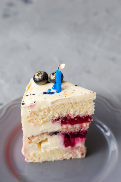 Slice of Birthday Cake with a lit candle over a gray background. Girl cake, Bakery and coocking concept - Photo, image