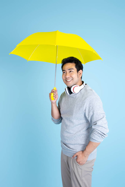 Asian man  holding yellow umbrella with blue background. - Foto, imagen