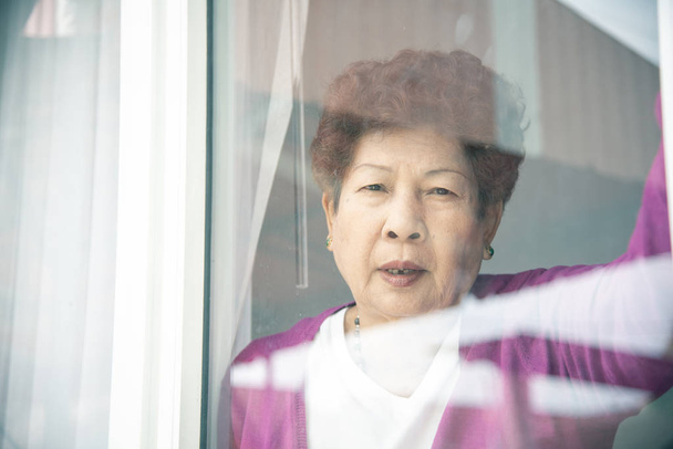 Asian senior woman standing near window and looking outdoor. - Foto, afbeelding