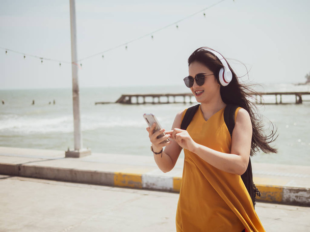 Boldog ázsiai nő hátizsák segítségével fejhallgató a strandon, li - Fotó, kép