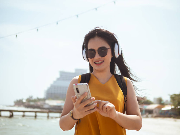 Happy Asian woman with backpack using headphone on the beach, li - Foto, imagen