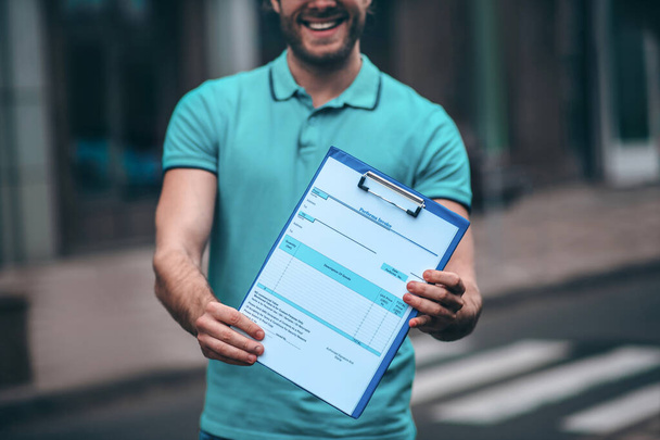 Bearded delivery man holding invoice after delivering product - 写真・画像