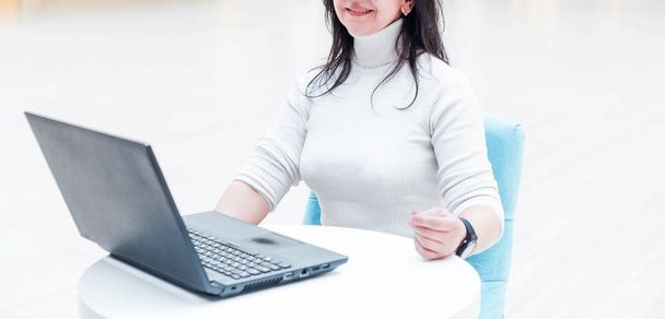 Stylish woman in a white sweater sits at a white table and works at a laptop - Foto, Imagem