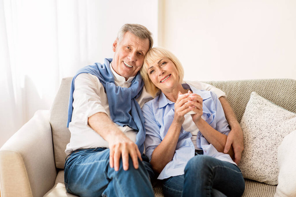 Happy mature couple sitting on sofa and embracing - 写真・画像