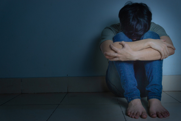 sad man hug his knee and cry sitting alone in a dark room. Depre - Fotografie, Obrázek