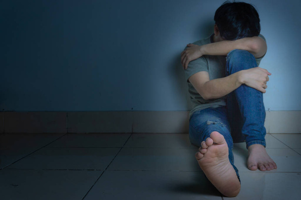 Trauriger Mann umarmt sein Knie und weint allein in einem dunklen Raum sitzend. depre - Foto, Bild