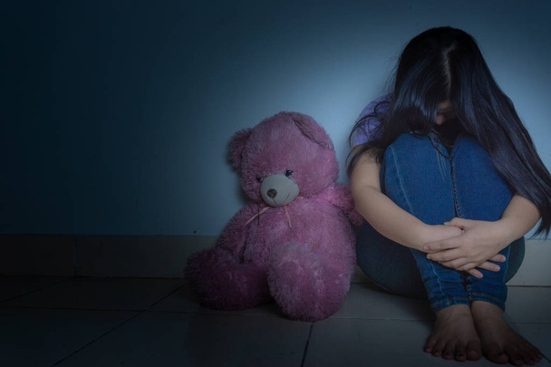 smutna kobieta przytula kolano i płacze siedząc z pluszowym miśkiem w ciemności - Zdjęcie, obraz