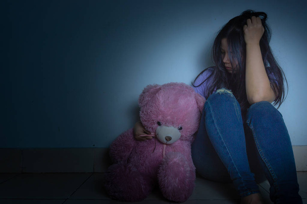 Üzgün kadın dizine sarıldı ve ağladı. Karanlıkta oyuncak ayıyla otururken. - Fotoğraf, Görsel