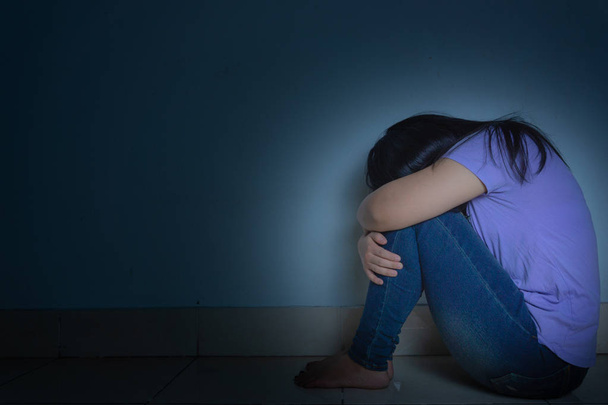 trieste vrouw omhelst haar knie en huilt alleen in een donkere kamer. Dep - Foto, afbeelding