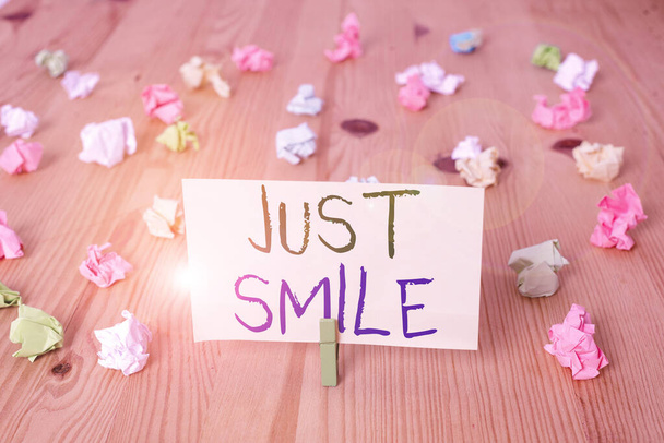 Conceptueel handschrift met Just Smile. Zakelijke foto tekst veronderstellen een gezichtsuitdrukking die plezier of amusement aangeeft Gekleurde verkreukelde papieren houten vloer achtergrond wasknijper. - Foto, afbeelding