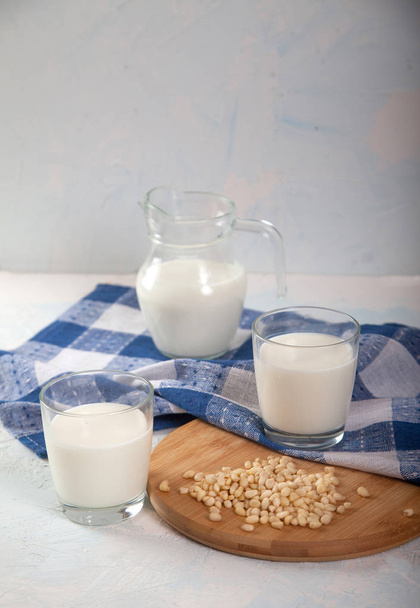 Vegetarian pine nut milk in glass cups and jug and blue linen napkin on white background. Vertikal. - Foto, afbeelding