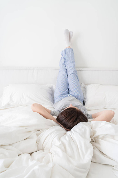 Nő pizsamában, felemelt lábbal és a feje alatt fekvő karokkal az ágyon. - Fotó, kép
