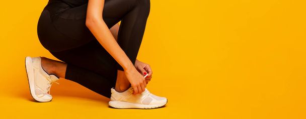 Sapatos de laço de senhora irreconhecíveis antes do treino de fitness, fundo amarelo, Panorama
 - Foto, Imagem