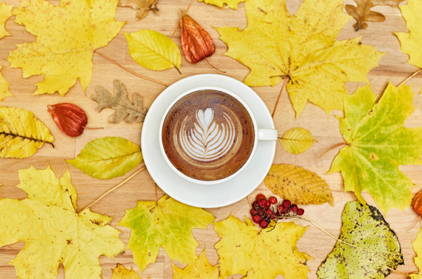 Composición plana de otoño con marco de corona de hojas secas y taza de café con leche sobre fondo de madera
.  - Foto, imagen