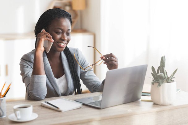 Современная деловая женщина из Африки, использующая мобильный телефон и ноутбук в офисе
 - Фото, изображение