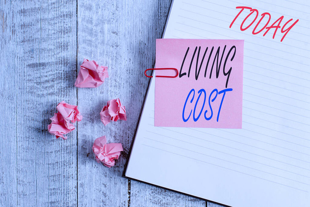 Writing note showing Living Cost. Business photo showcasing the amount of money that a demonstrating needs to sustain life Notebook stationary placed above classic wooden backdrop. - Photo, Image