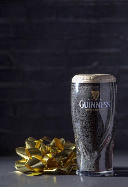 Κάλγκαρι Αμπ, Καναδάς. 26 Νοεμβρίου 2019. Ένα σκούρο ιρλανδικό ξηρό stout ποτήρι μπύρα με μια κορδέλα δώρο - Φωτογραφία, εικόνα