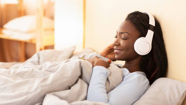 Afro-Mädchen mit Kopfhörer hört Musik im Bett, Panorama - Foto, Bild