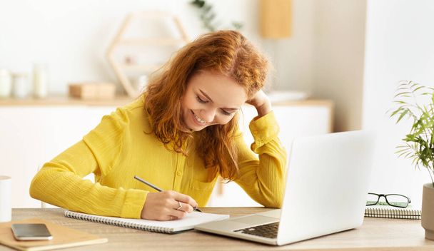 Business schedule. Smiling girl taking notes near laptop - Foto, Imagen