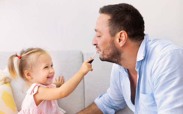 Little daughter doing makeup to her daddy - 写真・画像