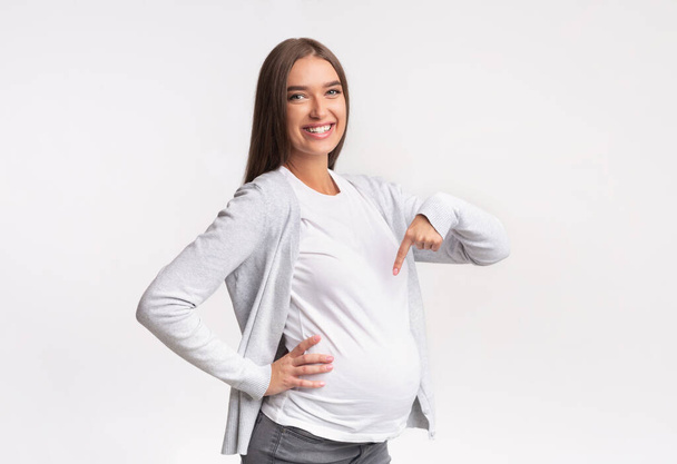 Pregnant Girl Pointing Finger At Belly Posing Over White Background - Photo, Image