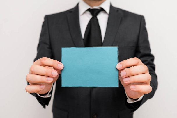 Männliche Menschen, die formale Arbeitskleidung tragen, halten altes Notizpapier in der Hand. Mann im Arbeitsanzug plus Krawatte im Büro-Look mit kleinem Zettelchen in der Hand - Foto, Bild