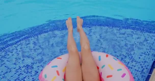 Top view on the legs of Caucasian woman in good shape while woman floating on the pink float in the swimming pool. - Materiał filmowy, wideo